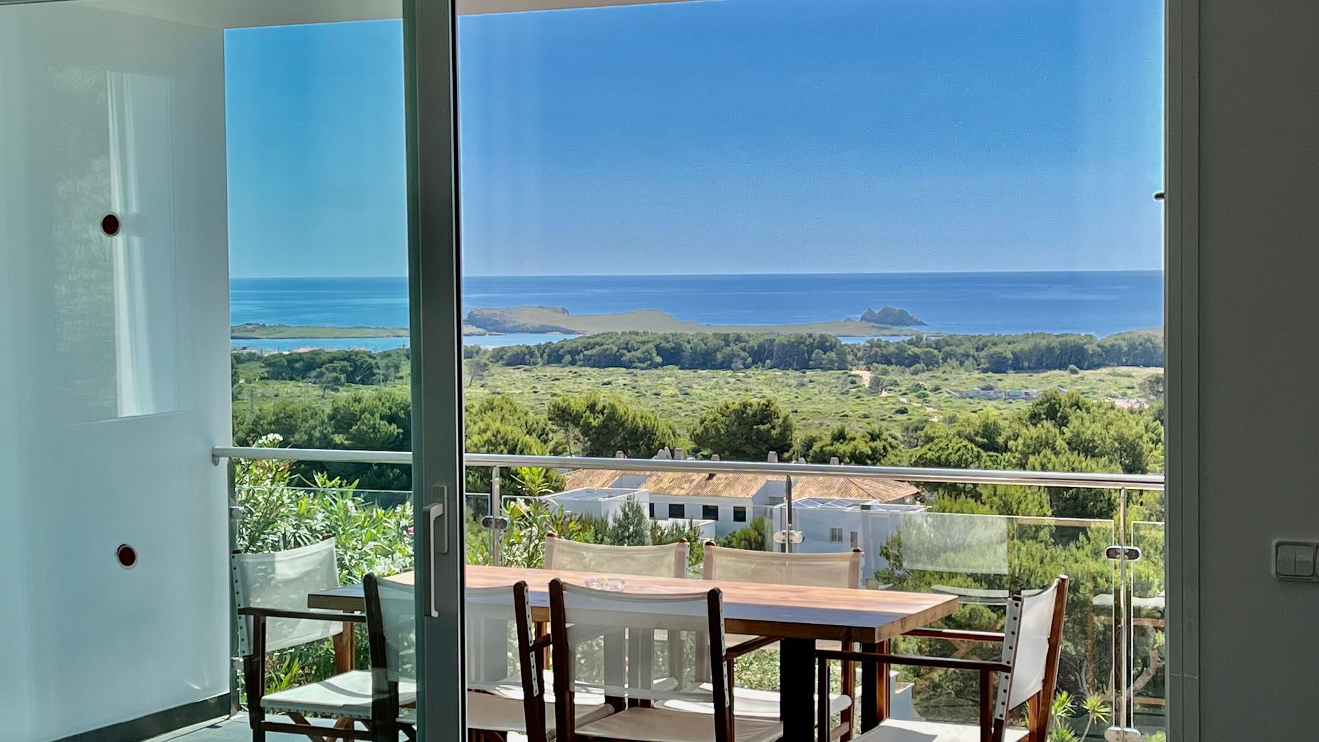 Balcón con vista al mar y paisaje verde a través de una puerta corrediza de vidrio.