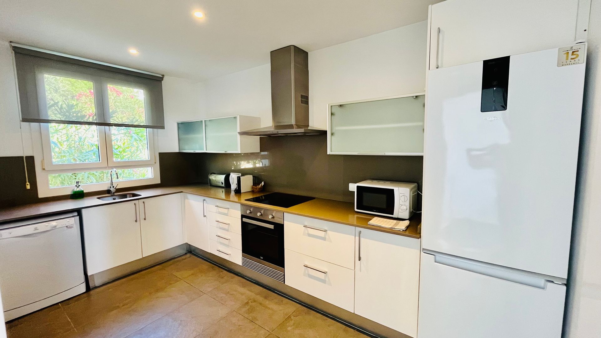 Cocina blanca moderna con electrodomésticos de acero inoxidable, encimera clara y ventana.