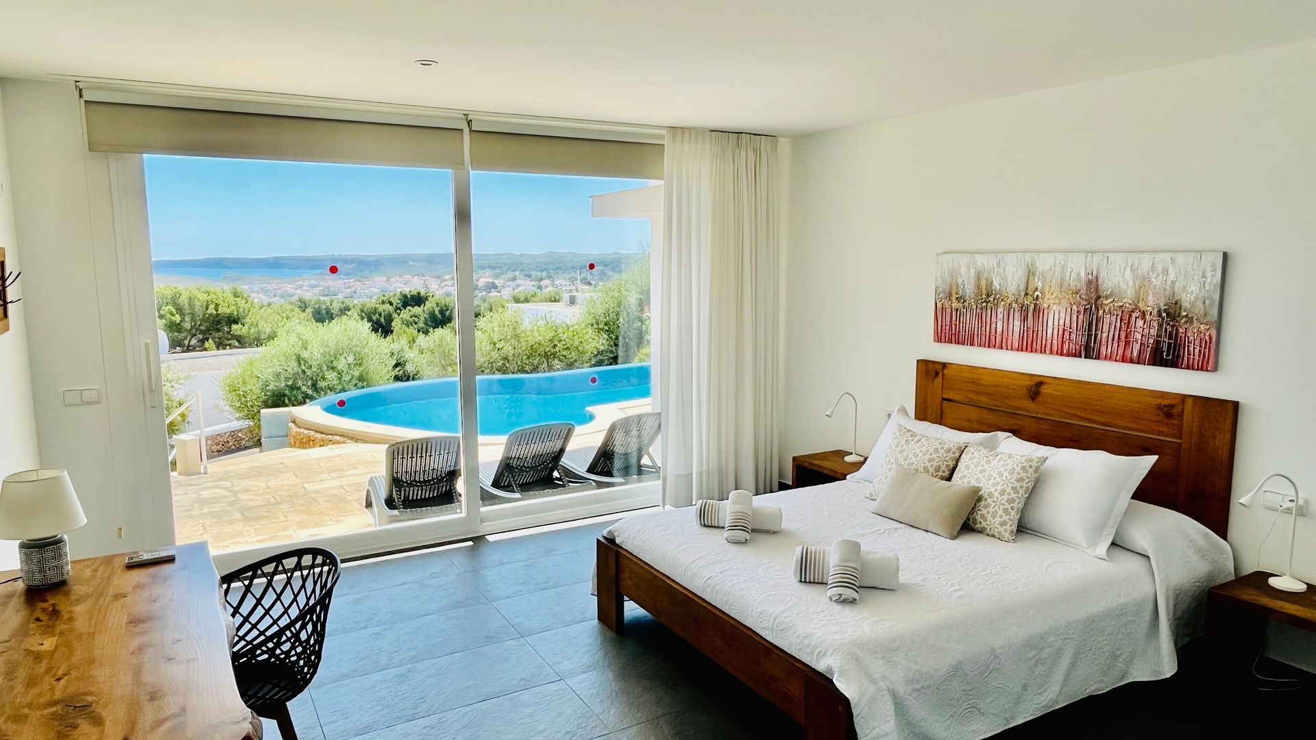 Dormitorio con cama, vista a la piscina y obras de arte.