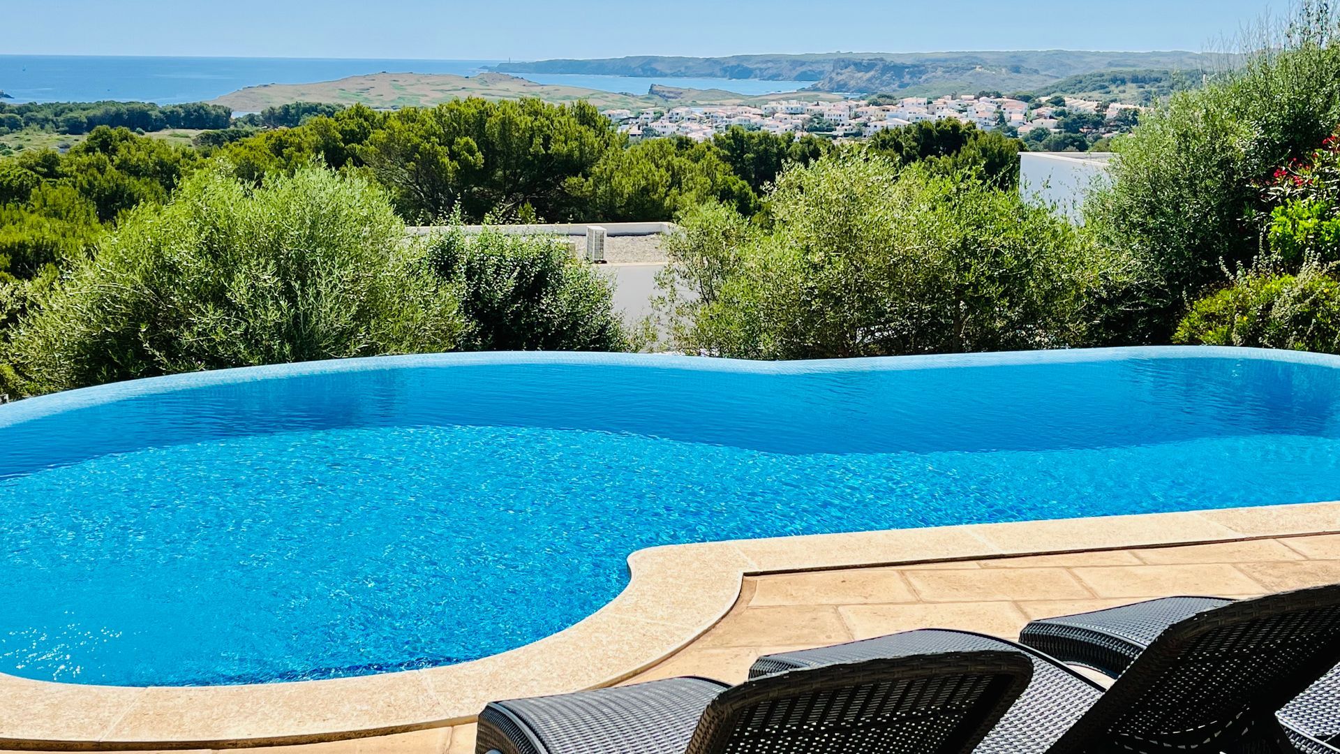Piscina infinita con agua azul cristalina con vista a una ciudad costera y al mar.