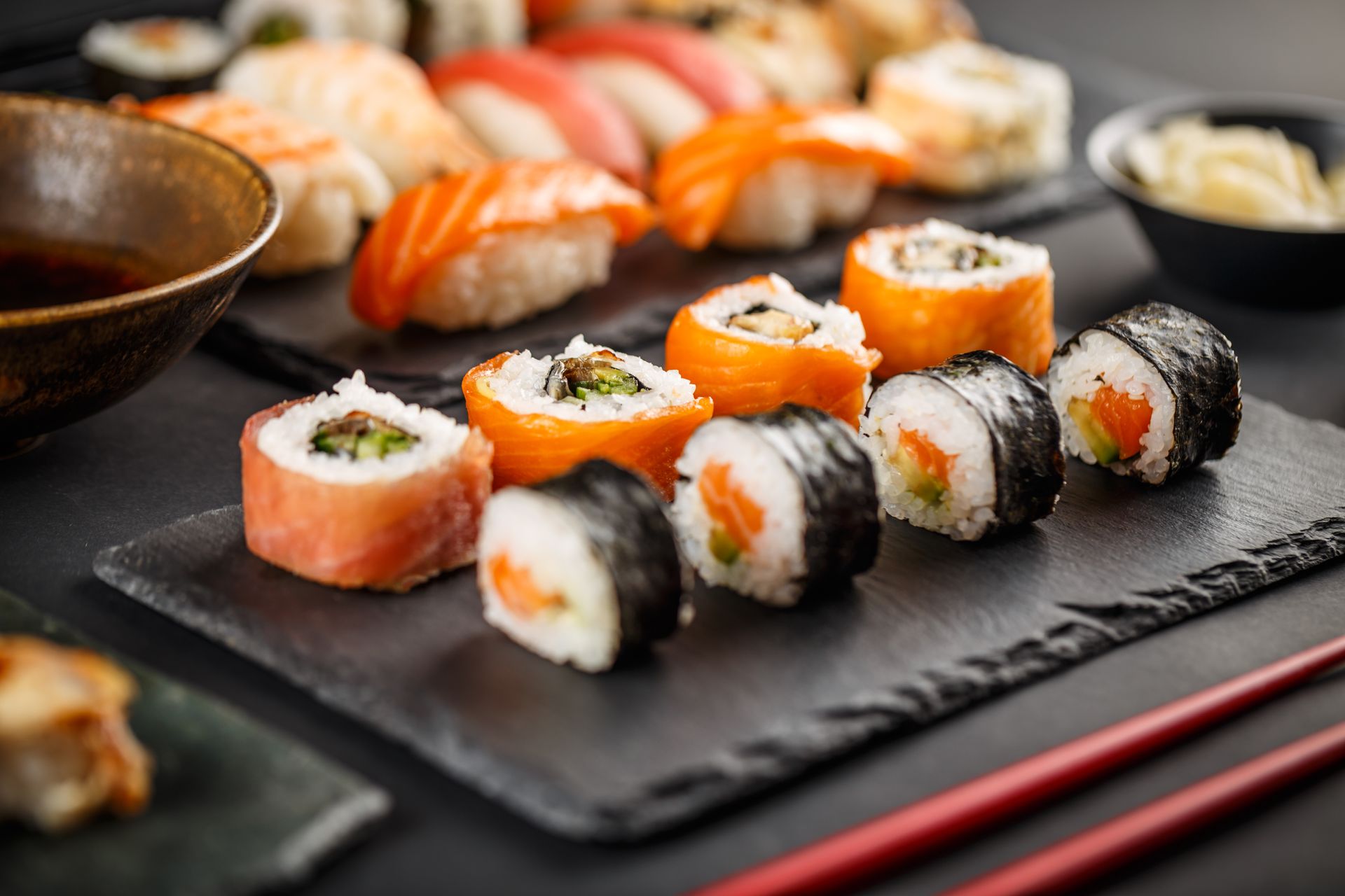 A plate of sushi with chopsticks and a bowl of soy sauce on a table.