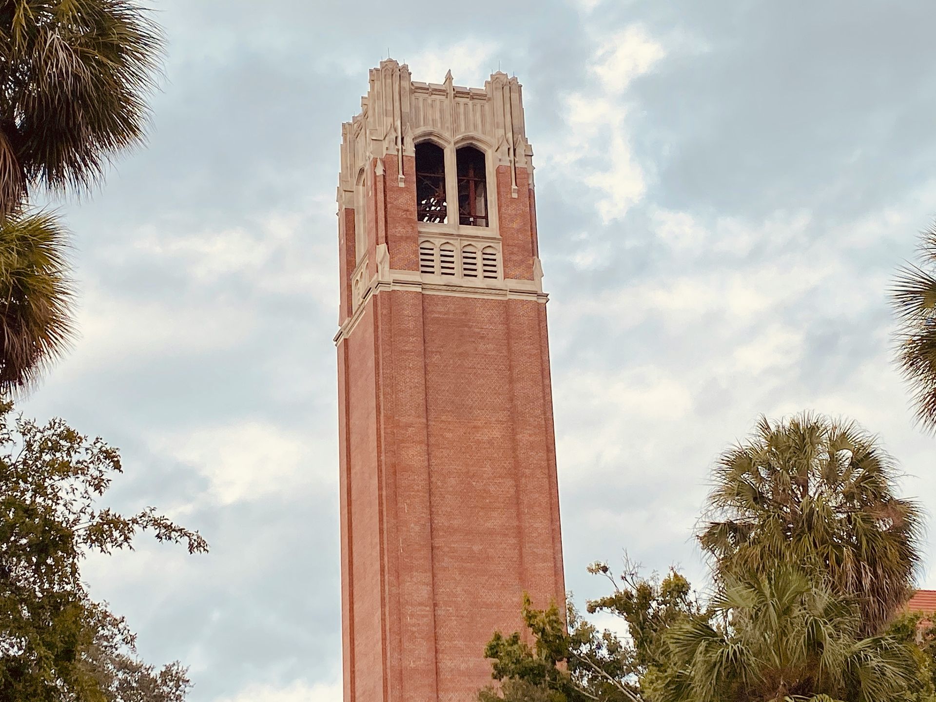 A large brick tower is surrounded by trees and a cloudy sky