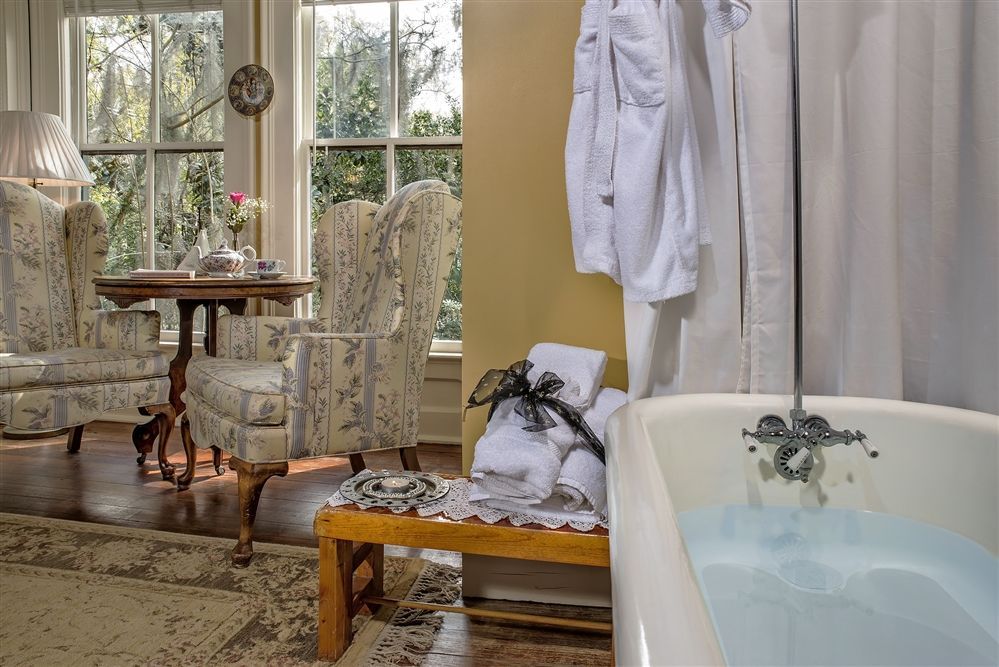 a bathroom with a bathtub , chairs , a table and a window .