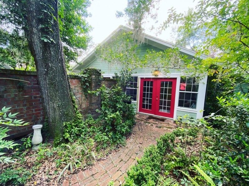 a small house with a red door is surrounded by trees and bushes .