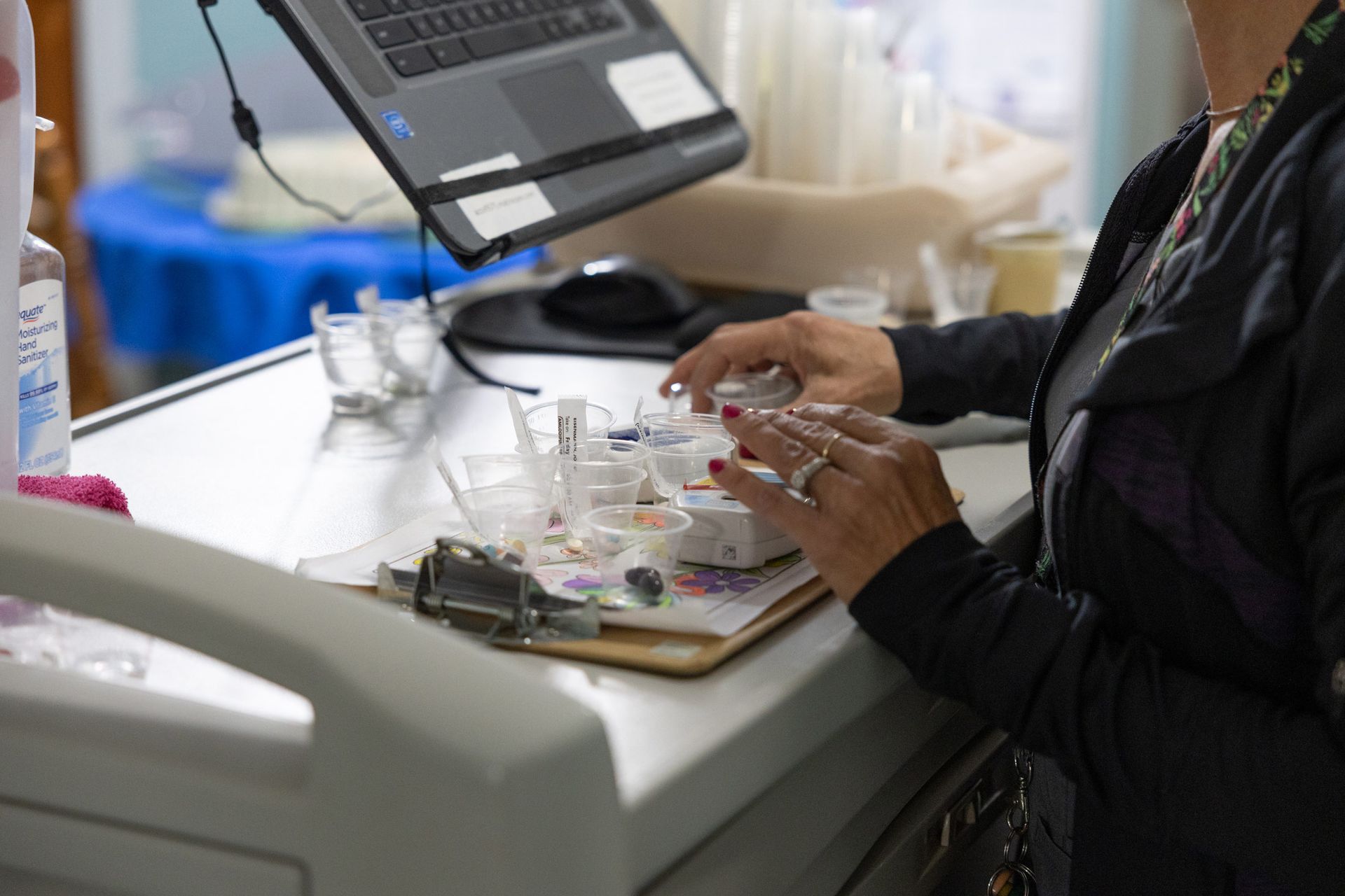 Nurse preparing medication in a hospital setting; a laptop and vials are on the desk.
