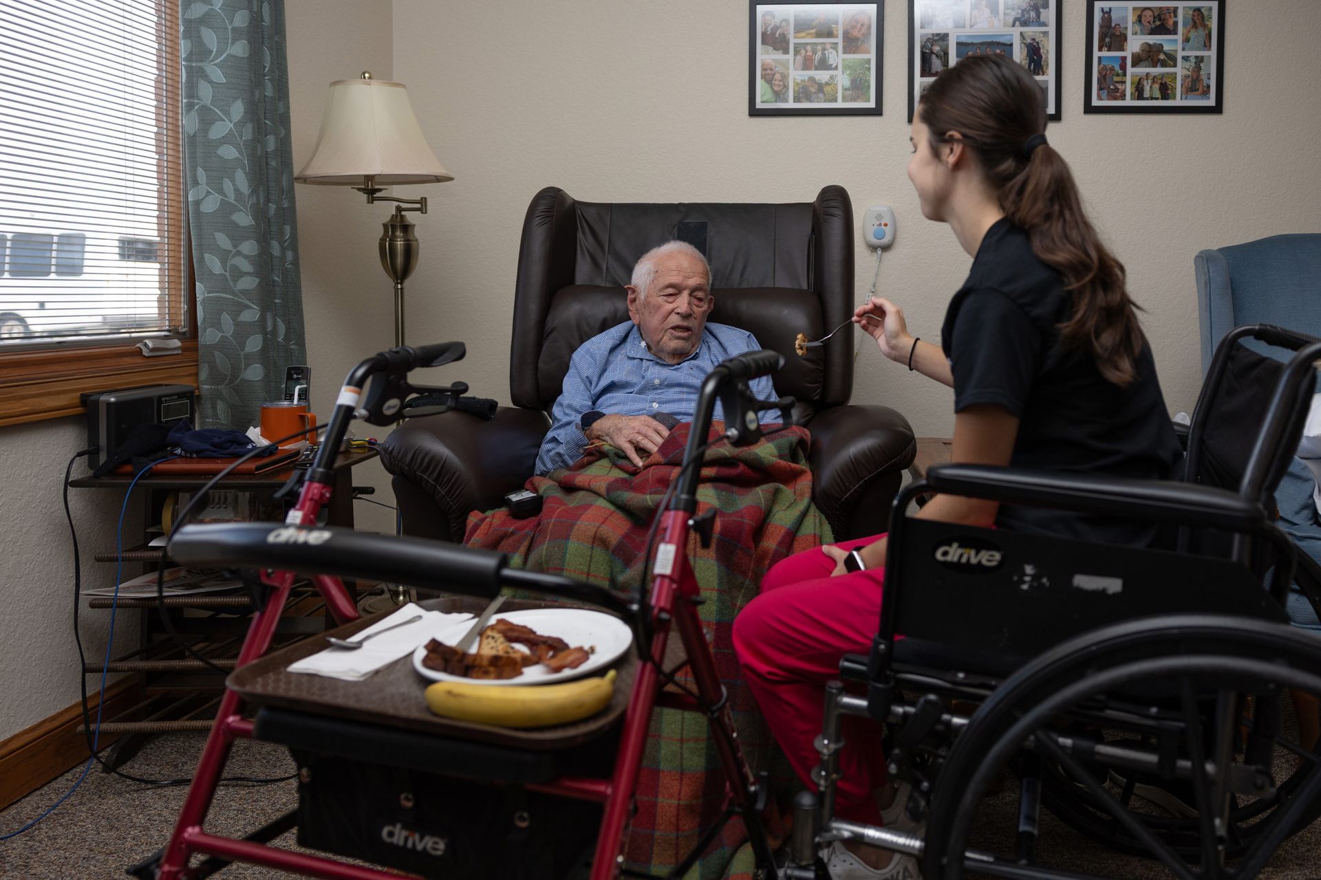 Elderly man in armchair with caregiver; inside a home.