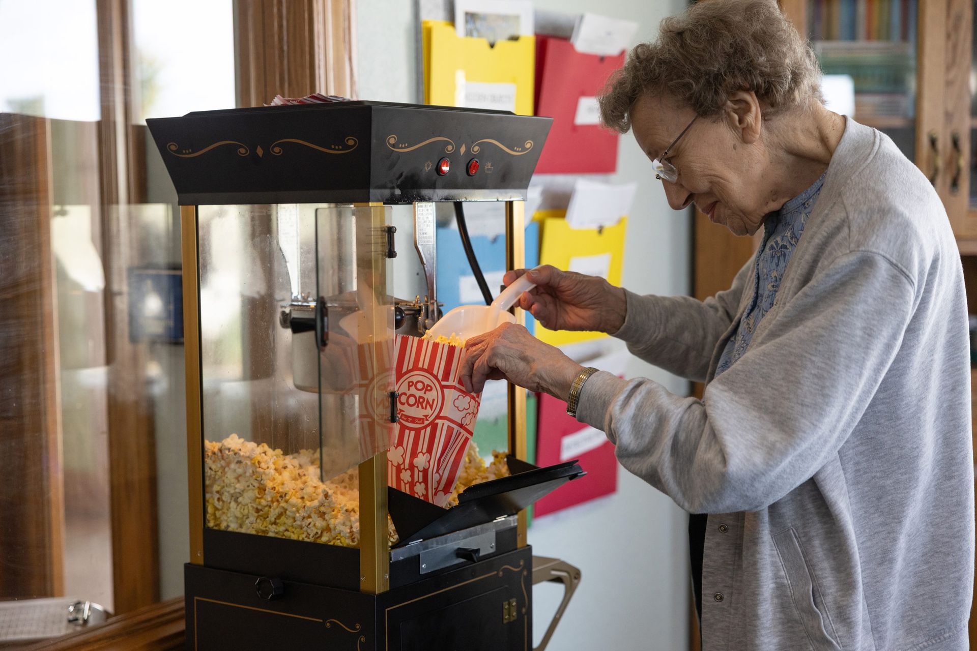 Elderly woman filling a popcorn bag from a popcorn machine, indoors.