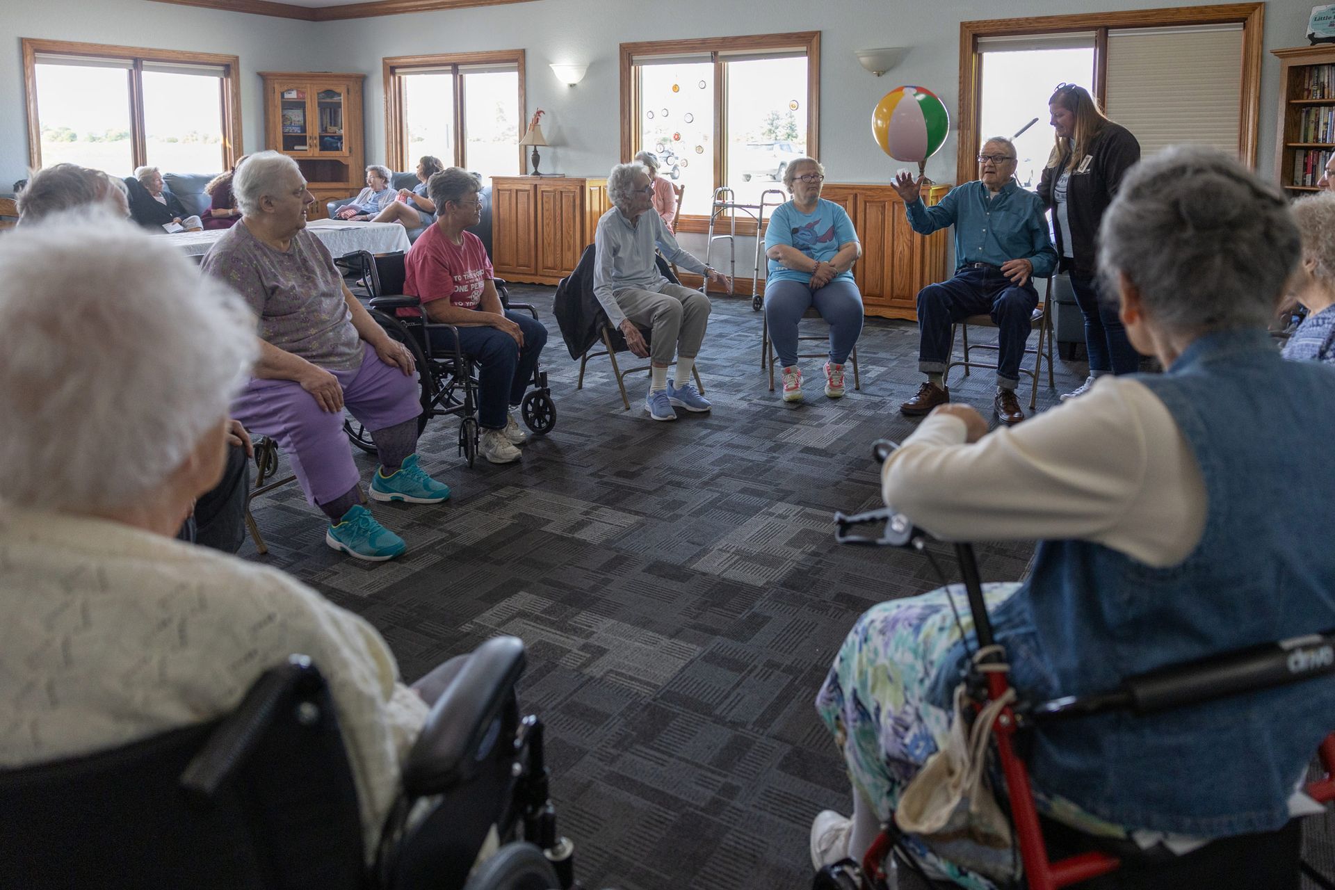 Group of seniors in chairs, playing with a beach ball in a well-lit room.