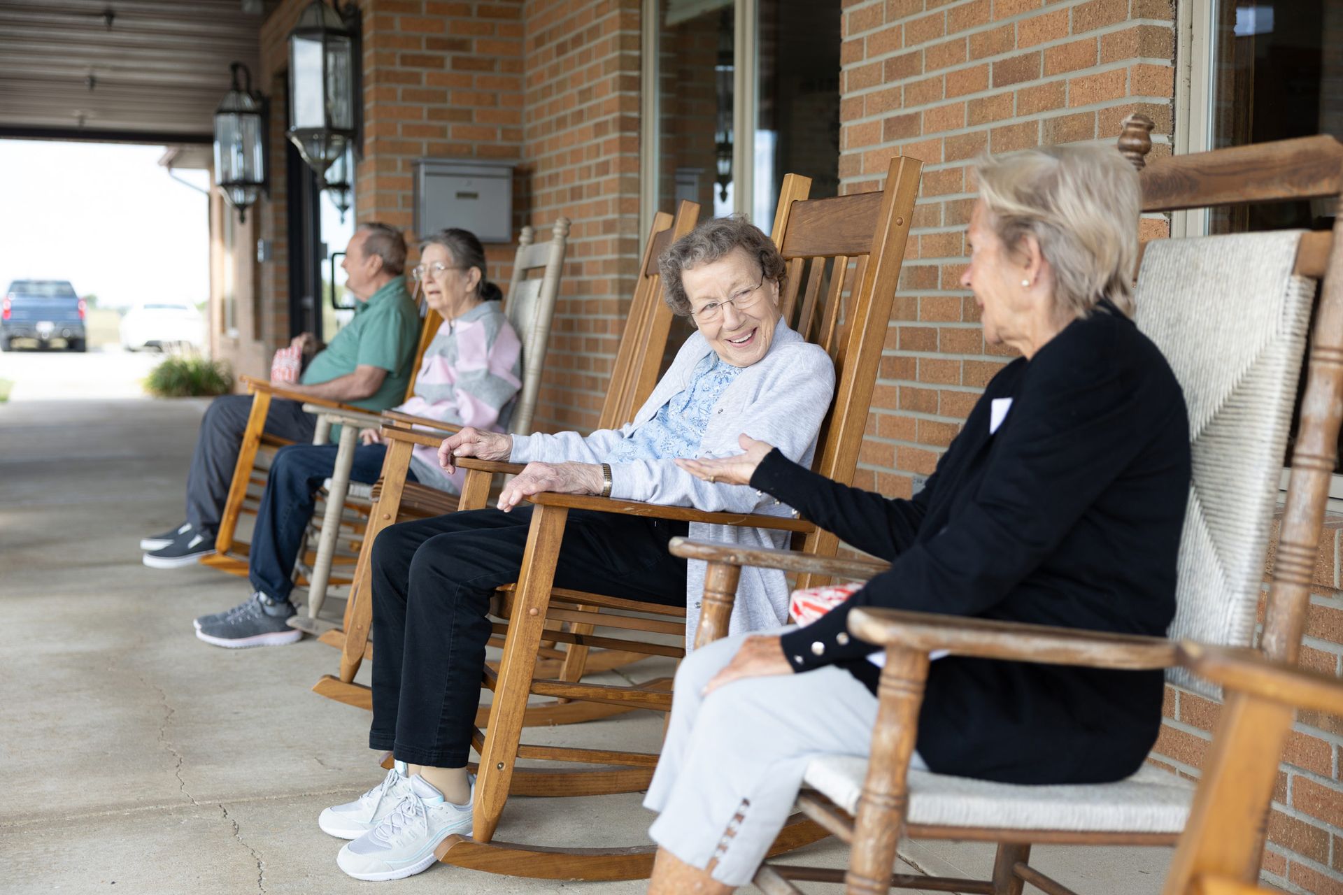 People in rocking chairs on a porch laughing. Brick building background.