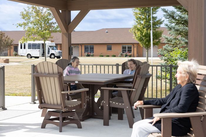 People sitting at outdoor table, covered patio. Buildings and van in background.