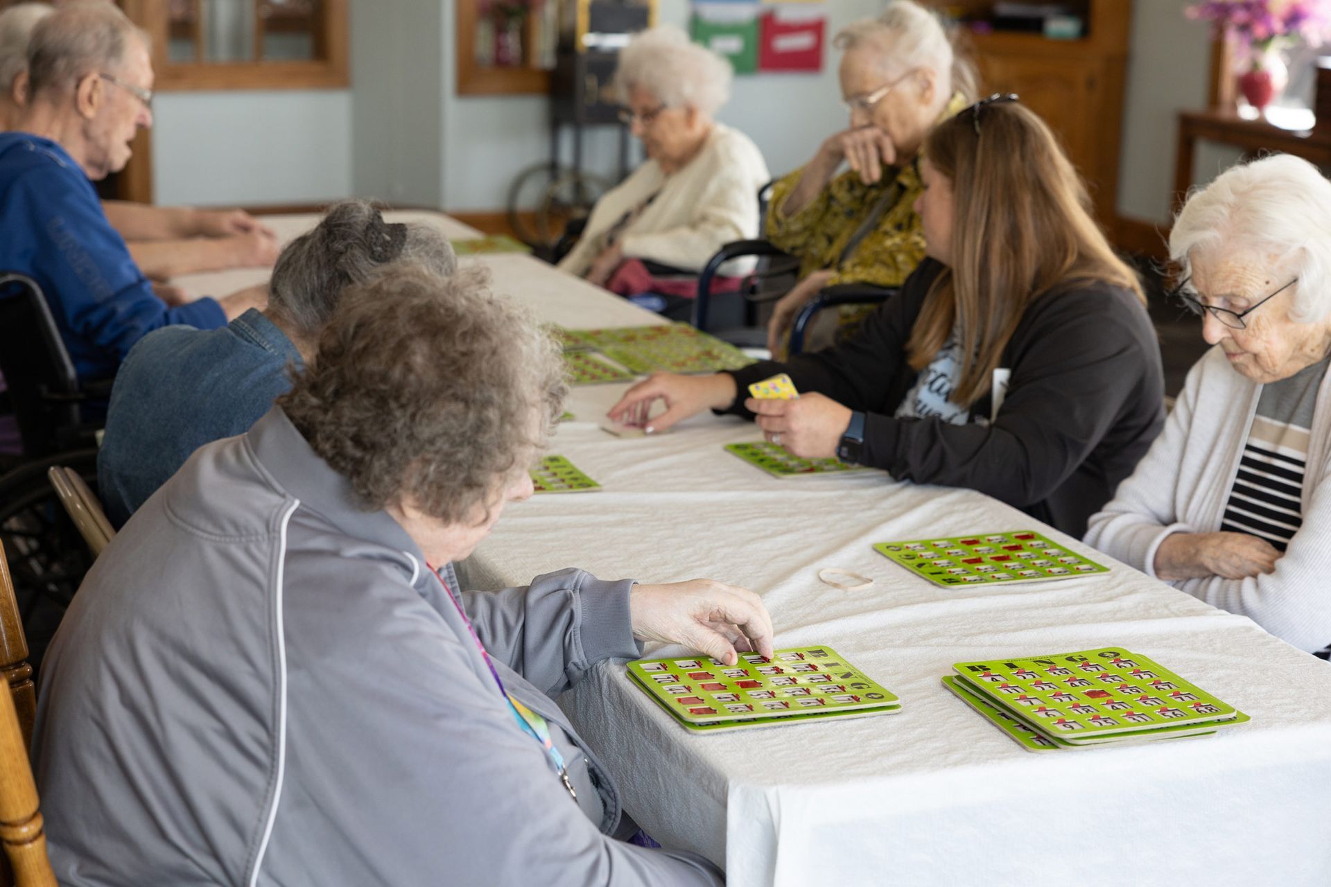 Seniors playing bingo at a table in a community center. A staff member calls out numbers.