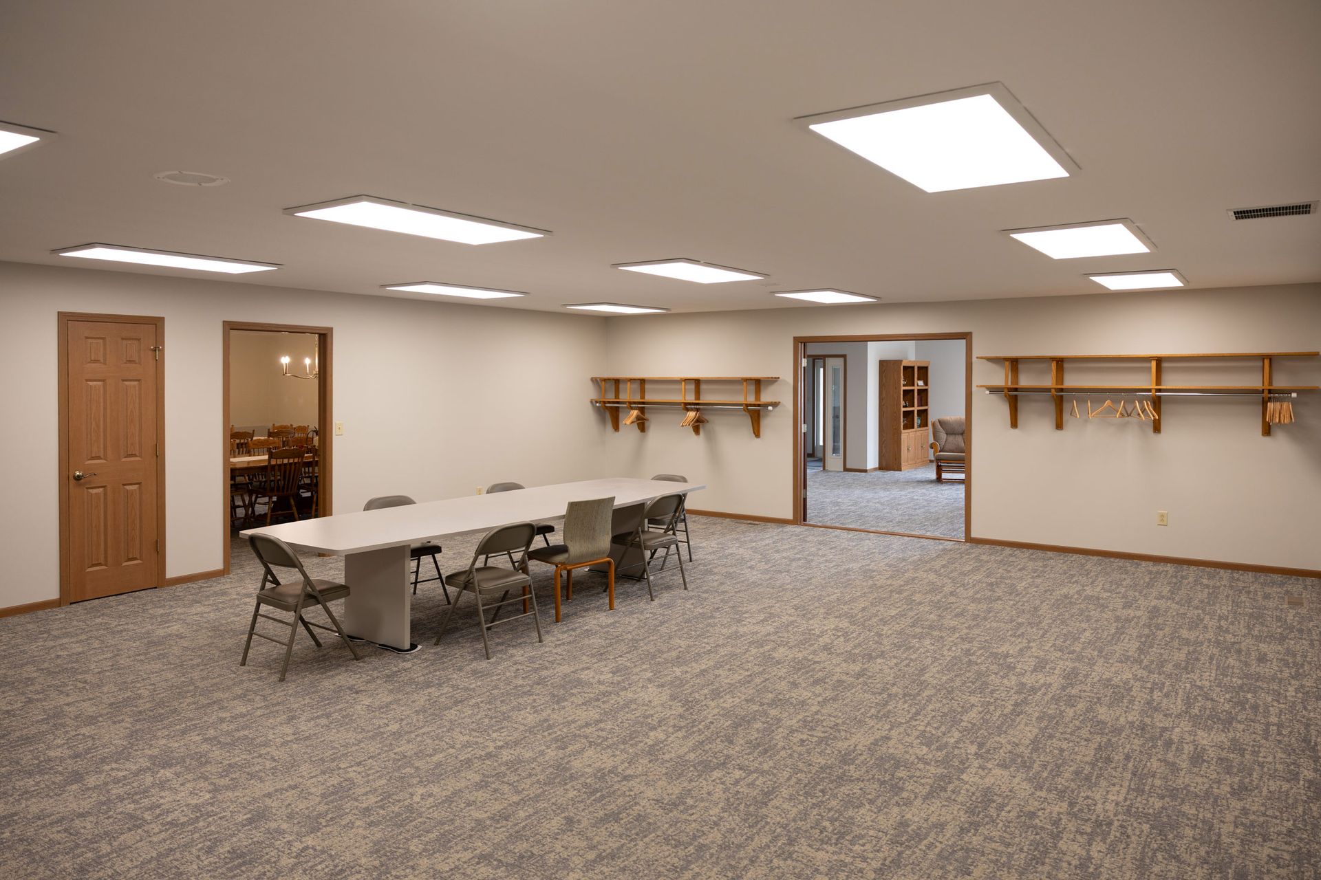 Empty meeting room with a long table and chairs, carpet, doors, and shelves.