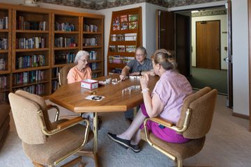 Three older adults playing a game at a table in a library.