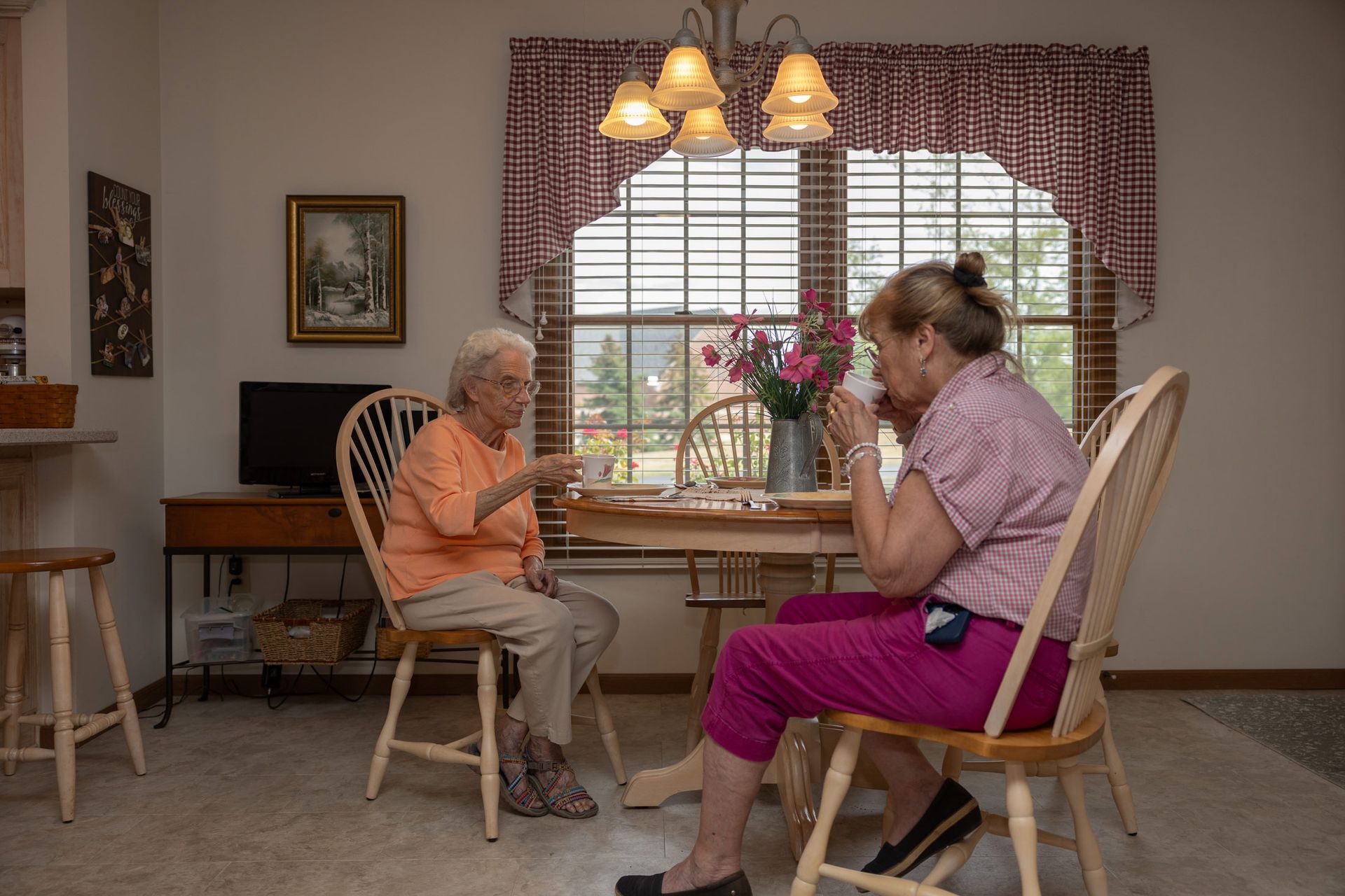 Two older women playing a game at a table in a home. Sunlight streams through the window.