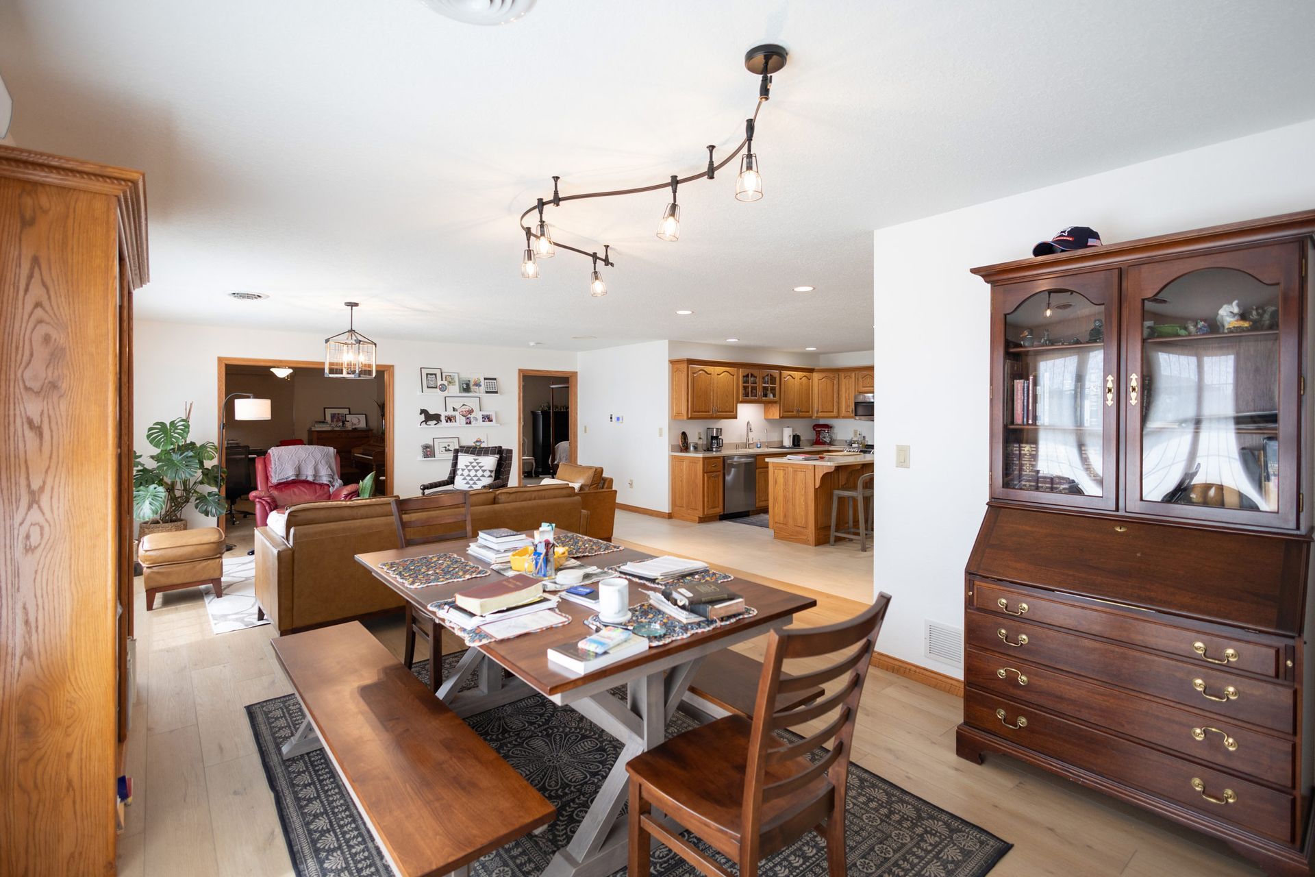Spacious dining room with wooden table, bench, chair, and hutch, leading into a living room and kitchen.