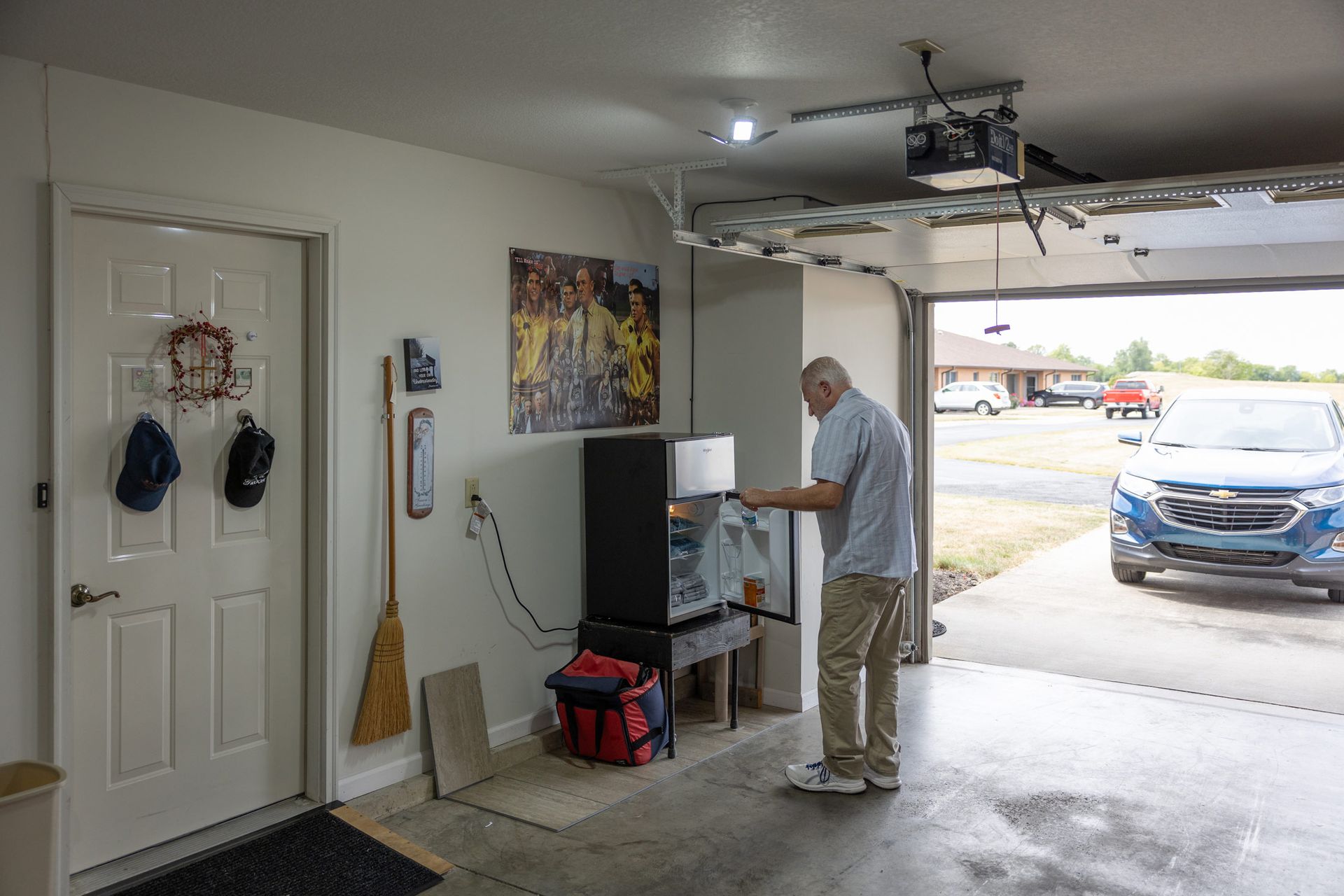 Man in garage, working on something near a black aquarium. Garage door open, car parked in front.