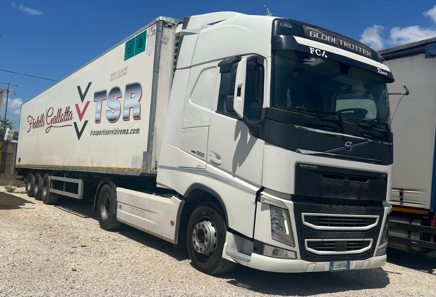 Autoarticolato bianco con rimorchio parcheggiato sulla ghiaia; logo aziendale 