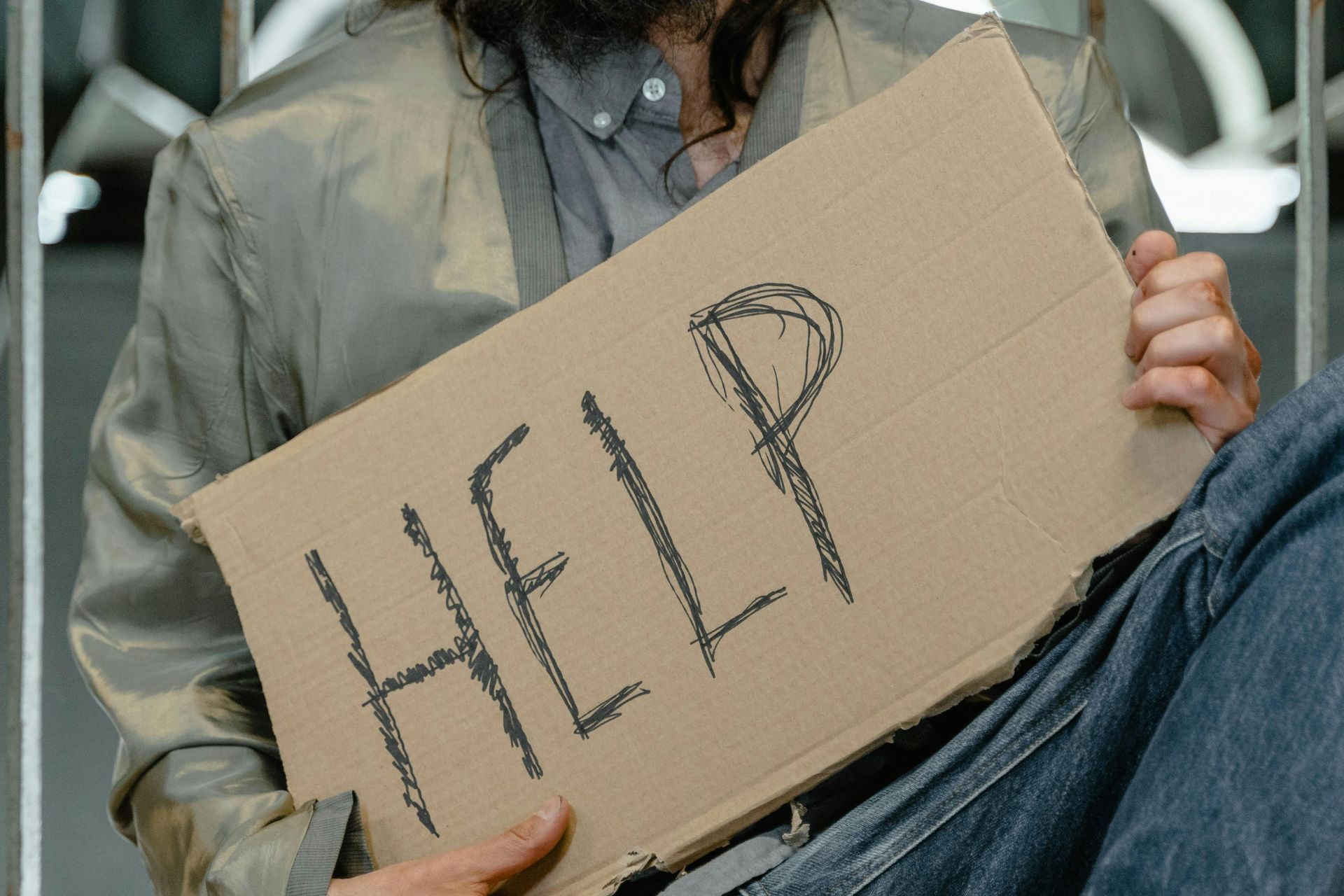 A person seated holding a cardboard sign that says 