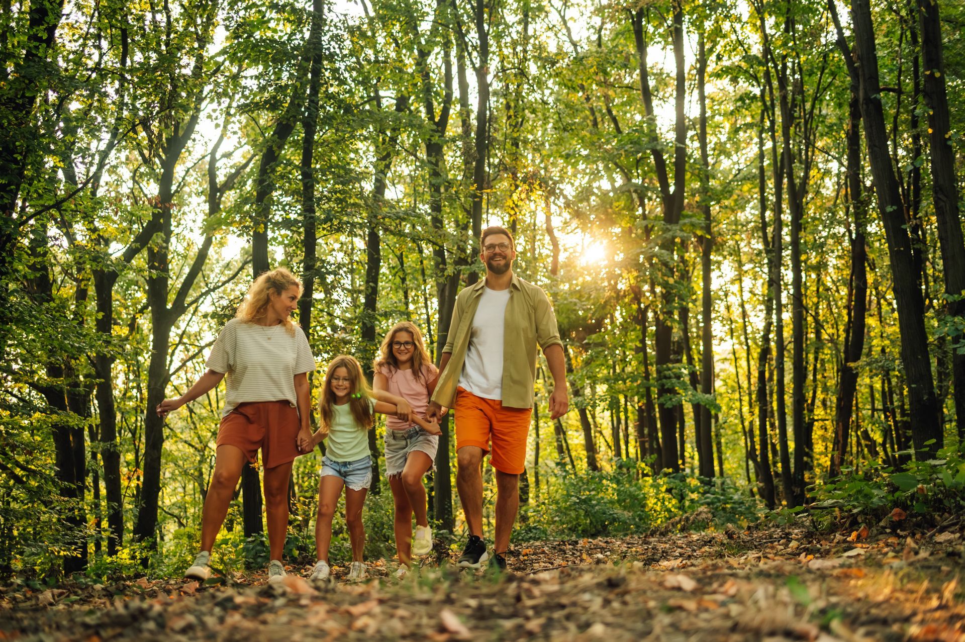 Family walks in sunlit forest, smiling.