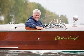 A man is sitting in the cockpit of a wooden boat.