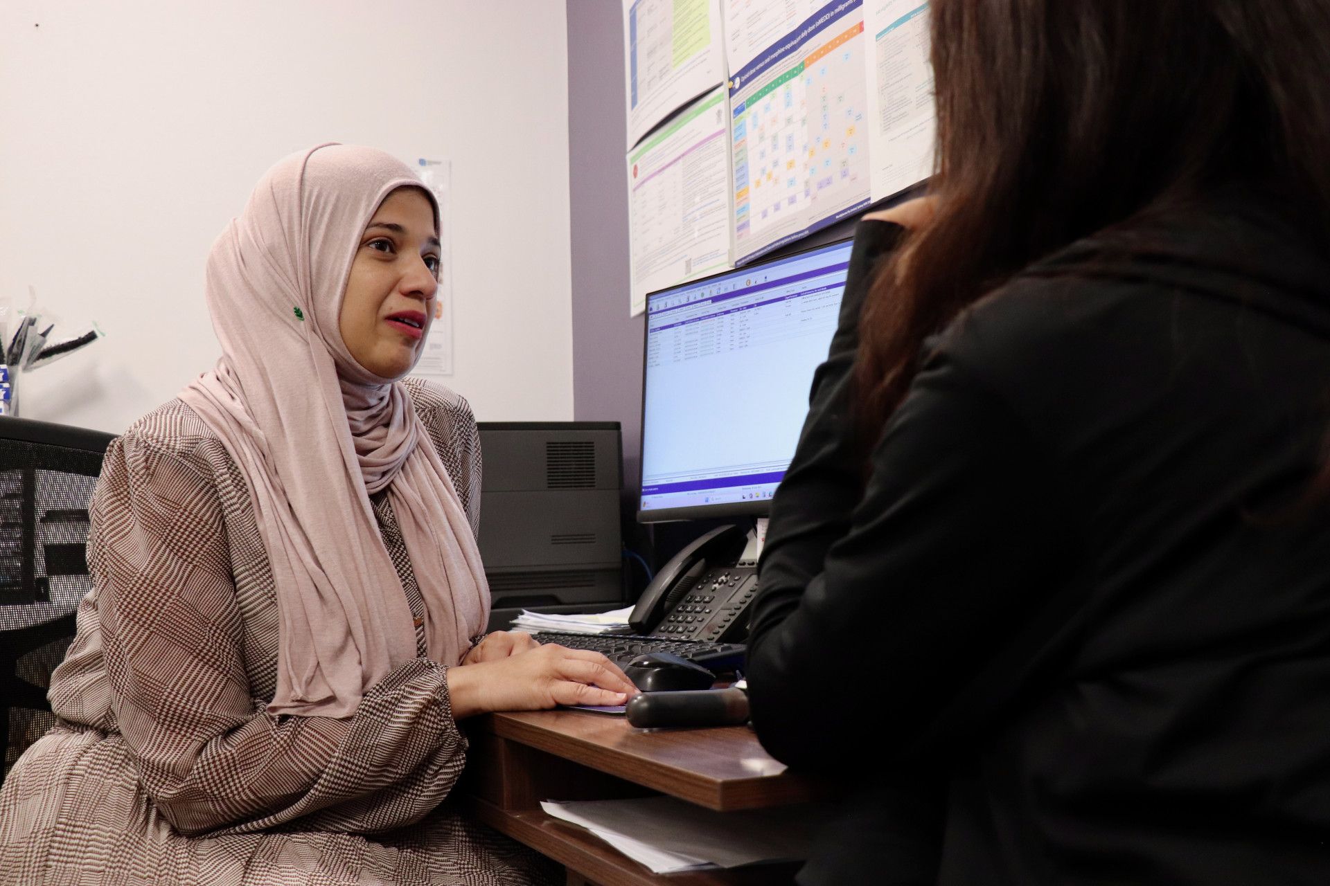 Woman in hijab talking to someone at a desk in an office.— One Stop Medical in Mackay, QLD