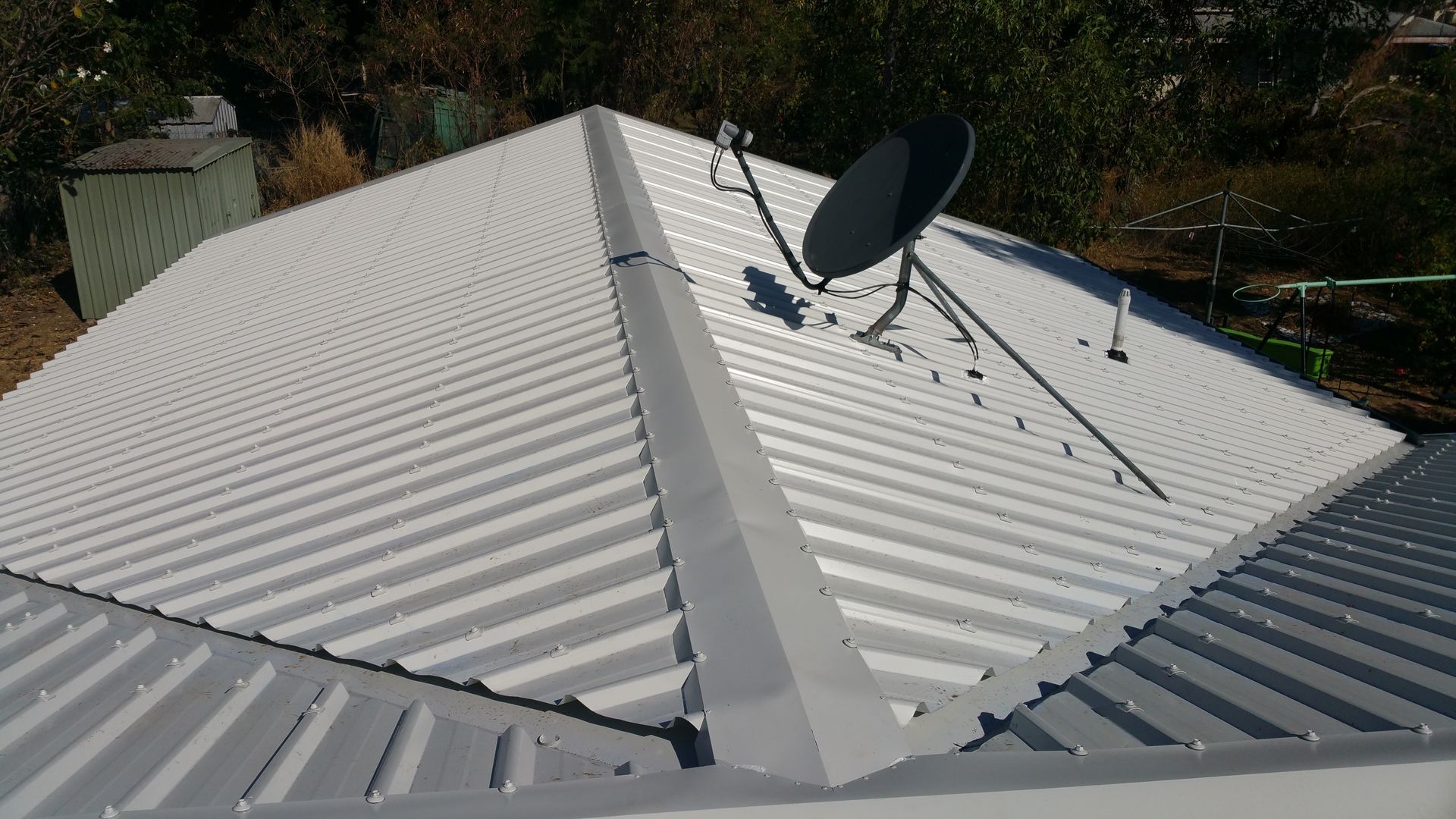 Two roofers in safety vests and hard hats repair a terracotta tile roof on a sunny day.