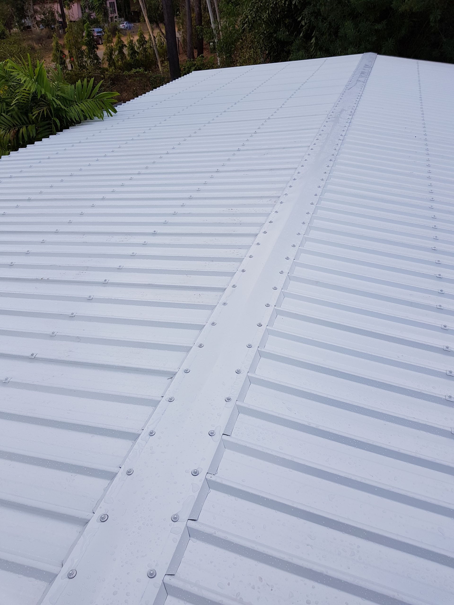 Roofer wearing yellow hardhat and vest, inspecting grey tile roof under a blue sky.