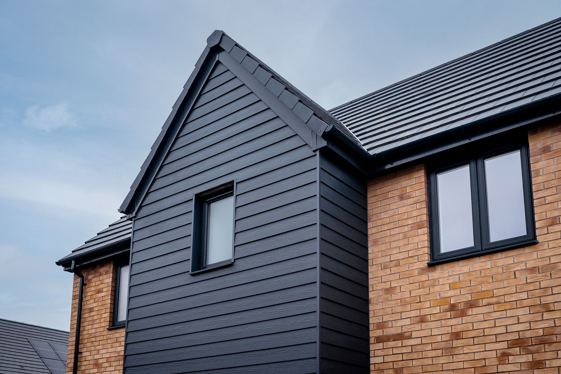 Brick house with dark siding and black window frames. Cloudy sky in background.