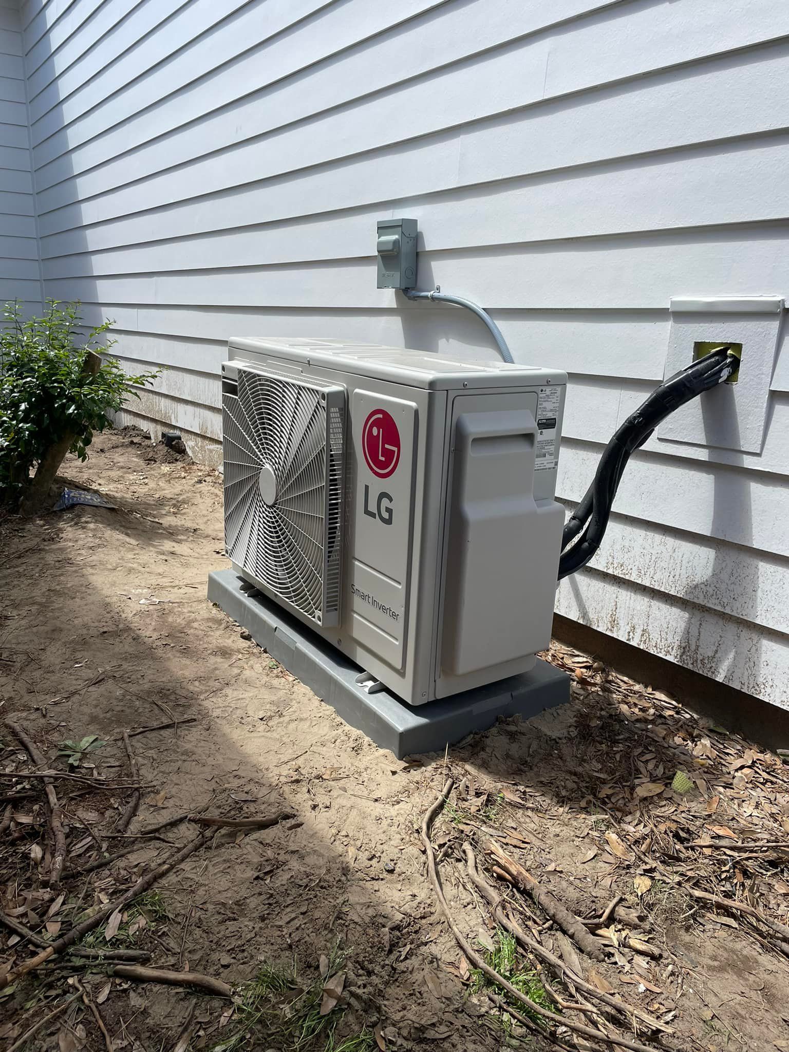 LG air conditioning unit installed on a concrete pad next to a white house with electrical connections.