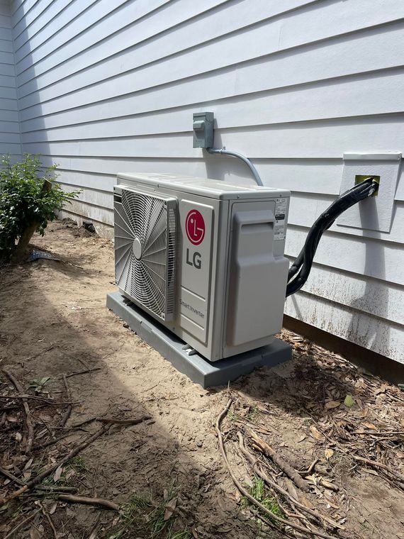 LG air conditioning unit on a concrete base, mounted on a white house siding, with electrical wiring.