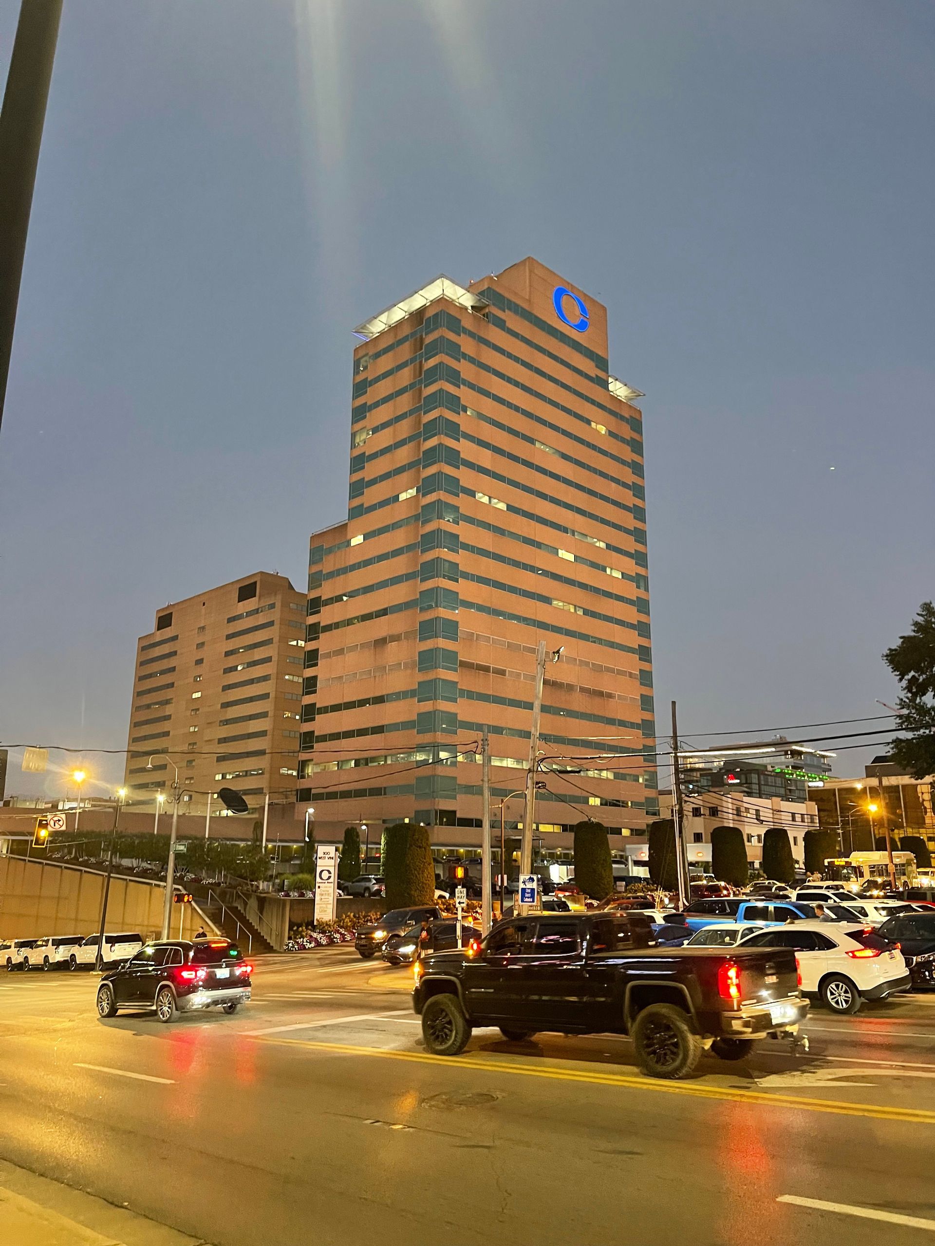 Tall brown office building with logo, traffic on street at dusk.