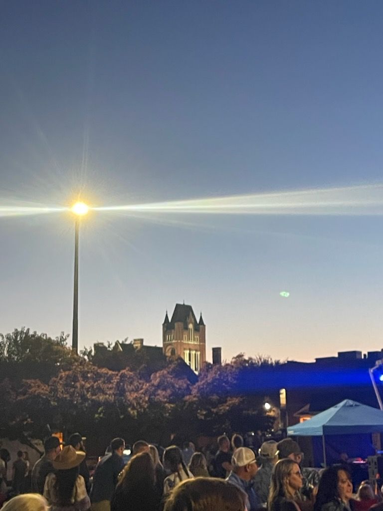Evening crowd near a gothic-style building, lit by a street lamp; blue sky overhead.
