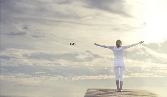 A woman is standing on a pier with her arms outstretched.