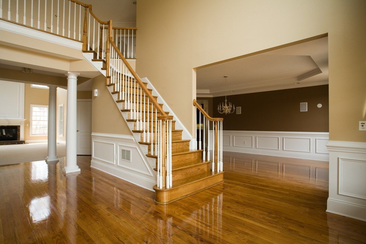 Wooden staircase in a spacious entry hall with hardwood floors. Beige walls, white molding, and an open doorway to another room.