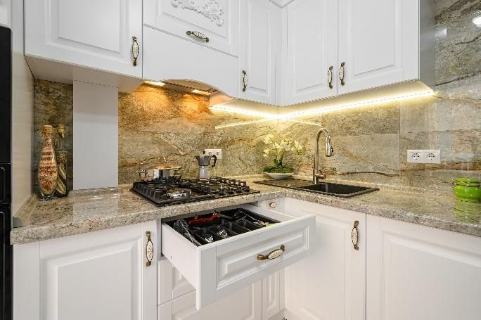 White kitchen with granite countertops and cabinets. A stovetop drawer is open, revealing burners.