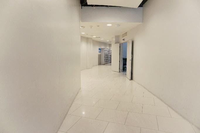 A white hallway with tiled floors and white walls, leading to a partially open doorway and a distant view.