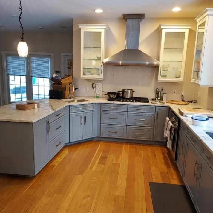 Spacious kitchen with gray cabinets, wooden floor, stainless steel range hood, and island with a marble countertop.