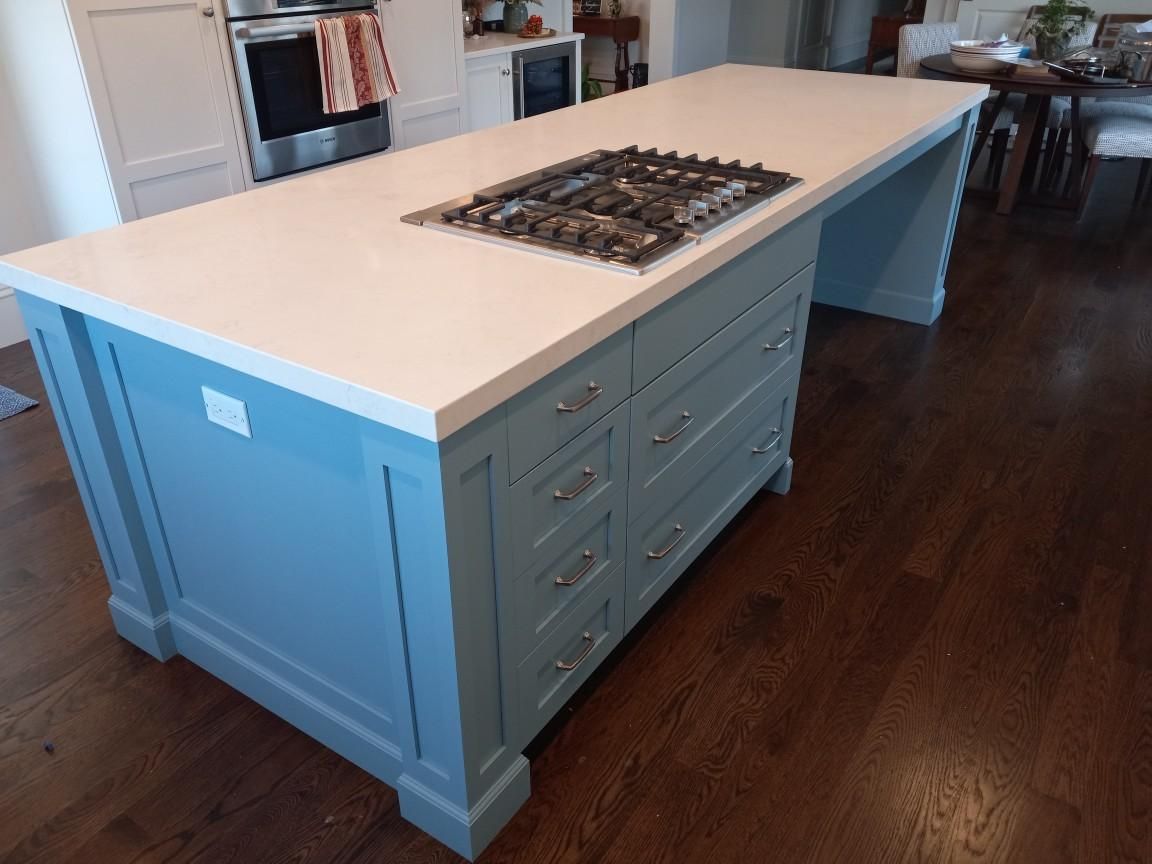 Blue kitchen island with a gas stovetop and light countertop in a kitchen with dark wood floors.