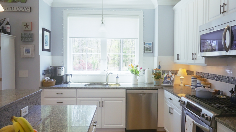 Bright kitchen with white cabinets, stainless steel appliances, and a window overlooking greenery. Granite countertops and tiled backsplash.