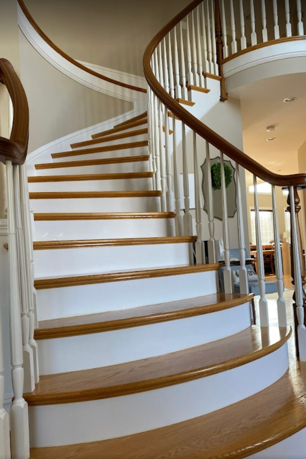 Curving wooden staircase with white risers, brown treads, and a wooden handrail.