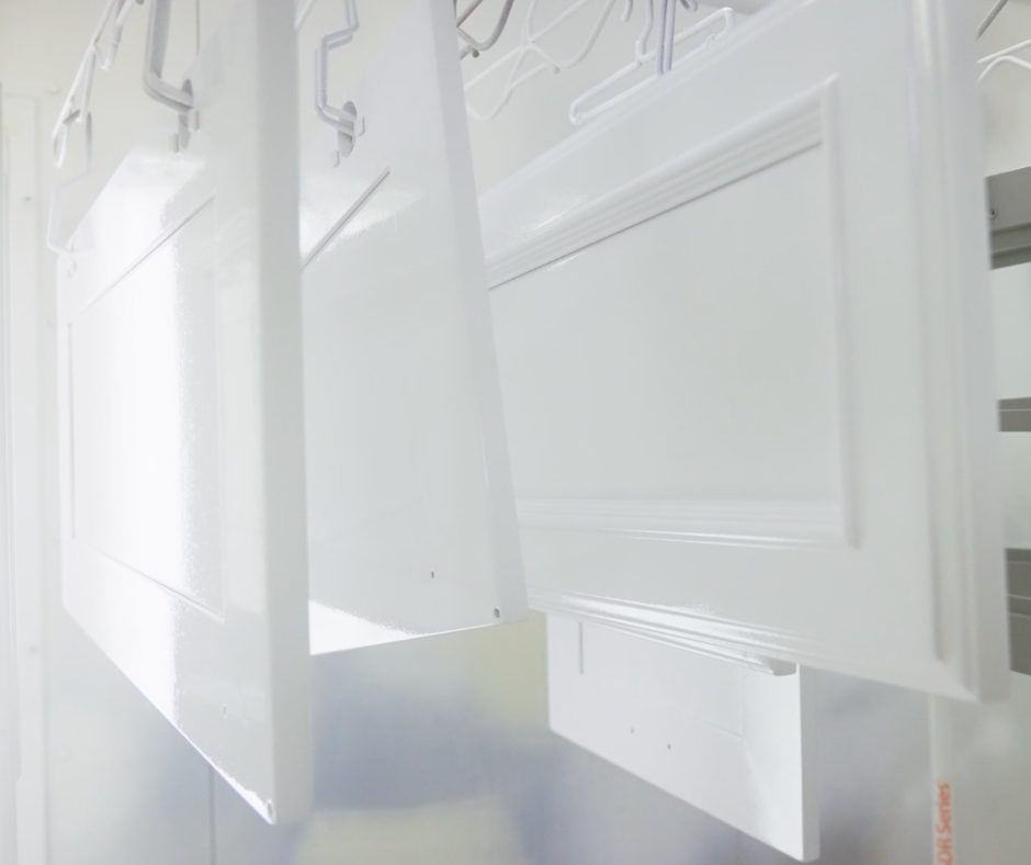 White cabinet doors hanging in a spray booth, freshly painted and awaiting drying.