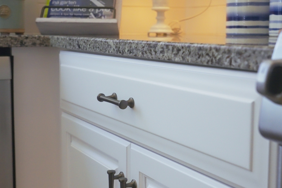 White kitchen cabinets with dark hardware, granite countertop, and a light-colored backsplash.
