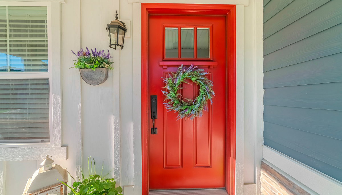 Bright red front door with a green wreath and purple flowers, framed by white and blue siding.