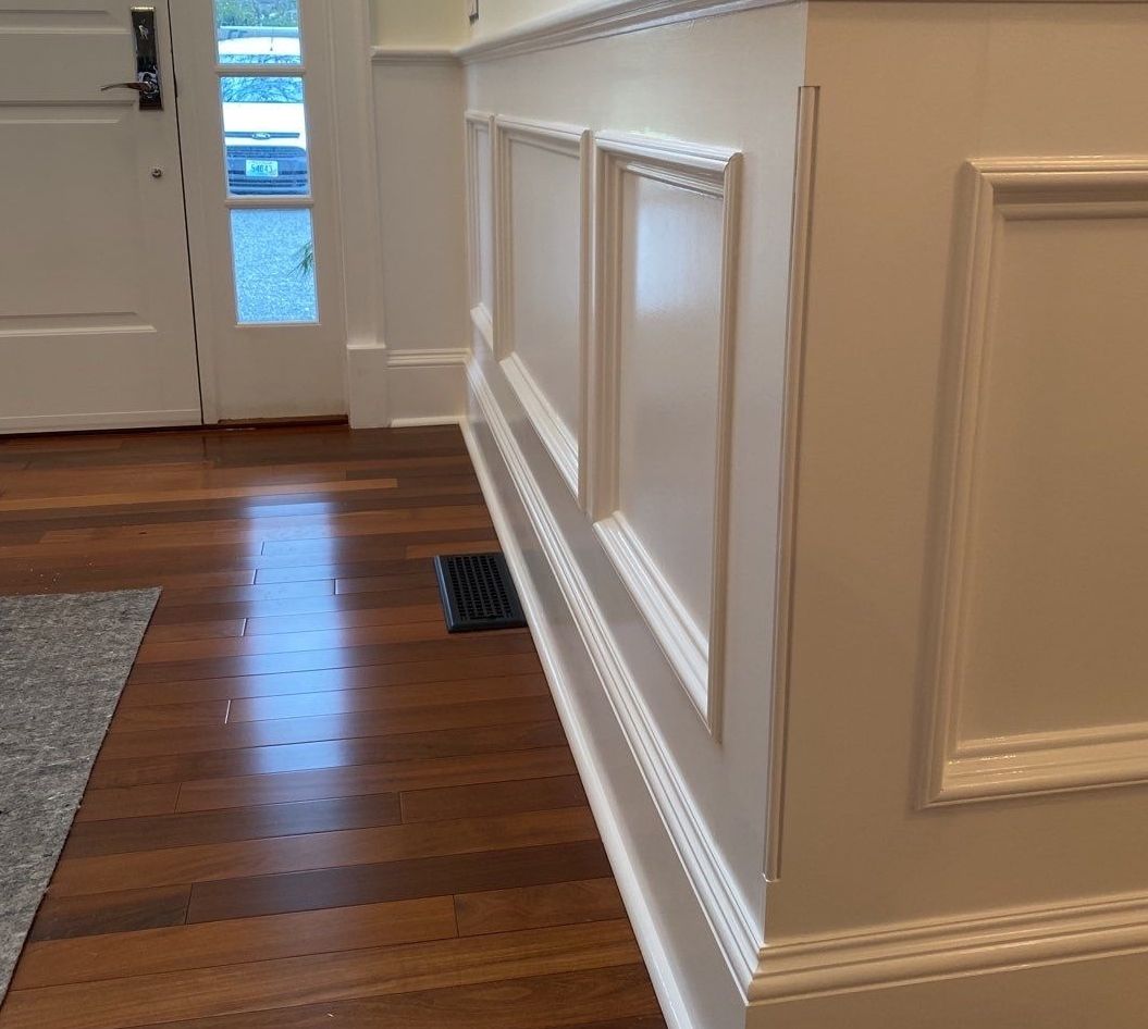 White wainscoting along a wall with dark wood flooring. A door is visible in the background.