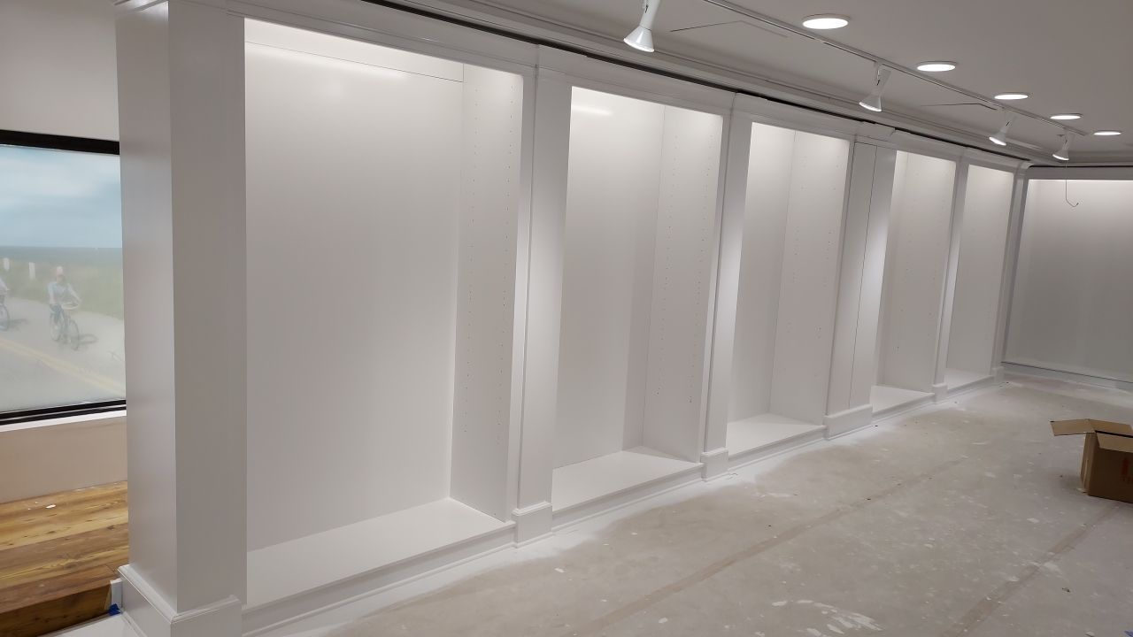 Empty white display niches built into a wall in a store. The floor is covered in protective sheeting.