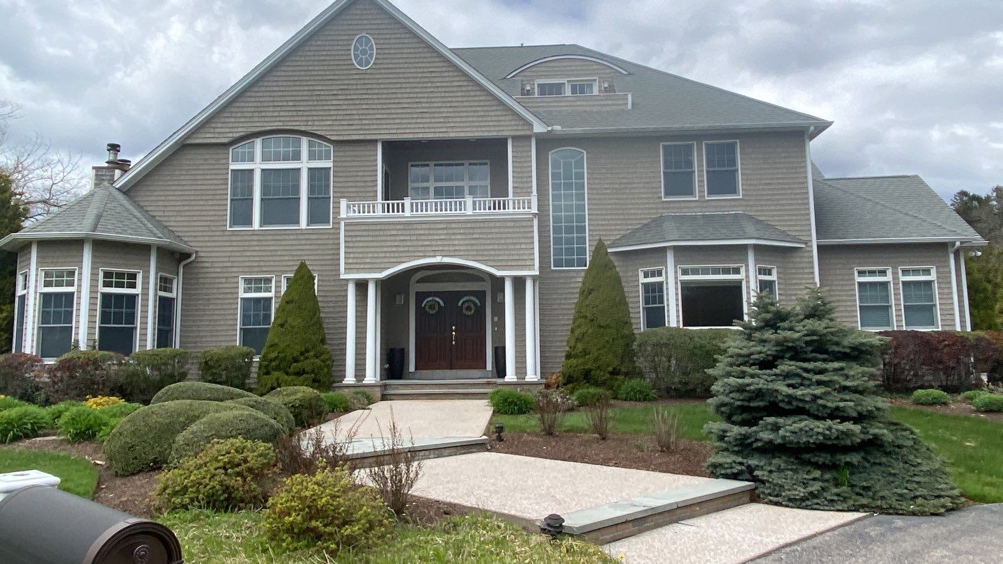 A large, two-story gray house with white columns, a curved front walk, and landscaping on a cloudy day.