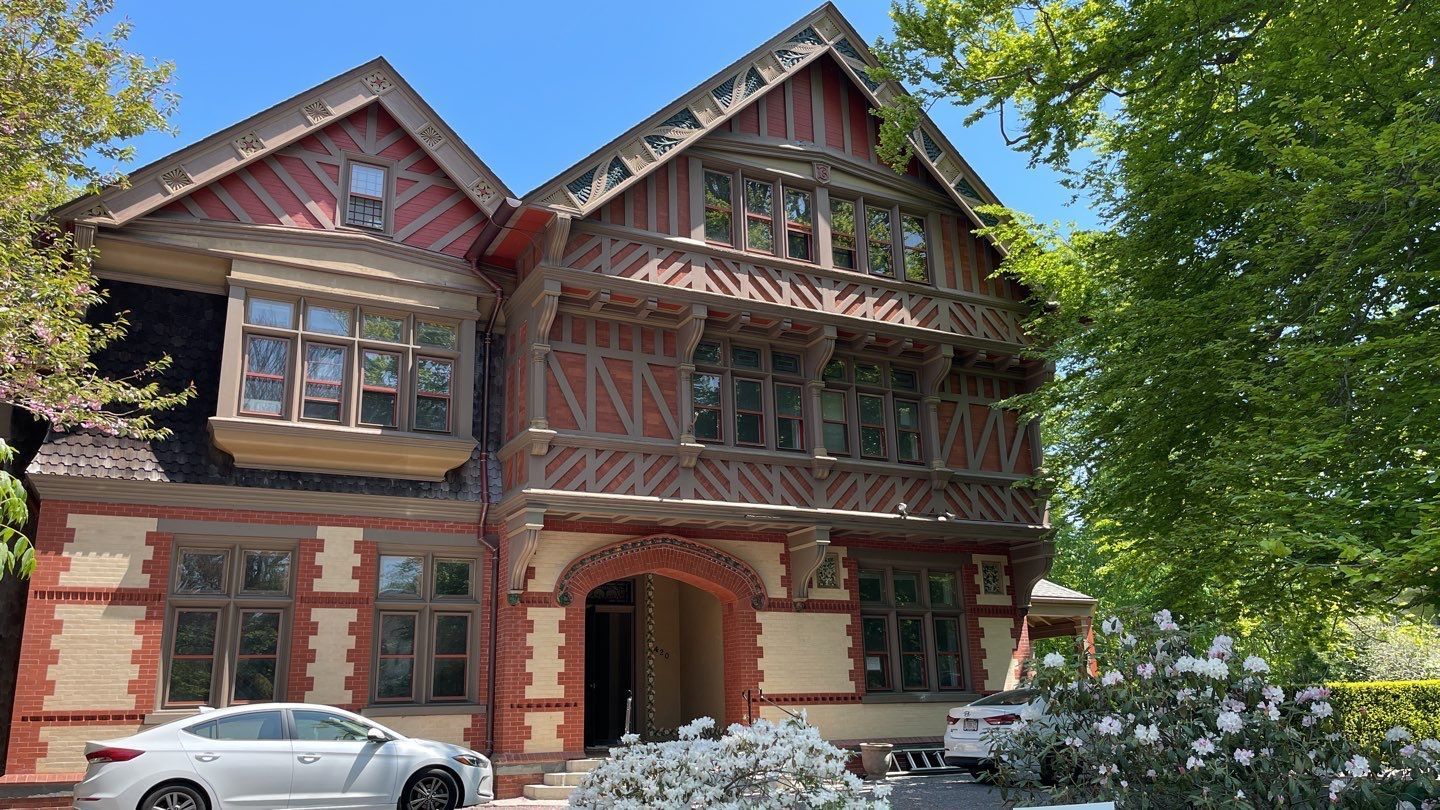 Tudor-style house with red brick, brown trim, and many windows. A white car is parked in front.