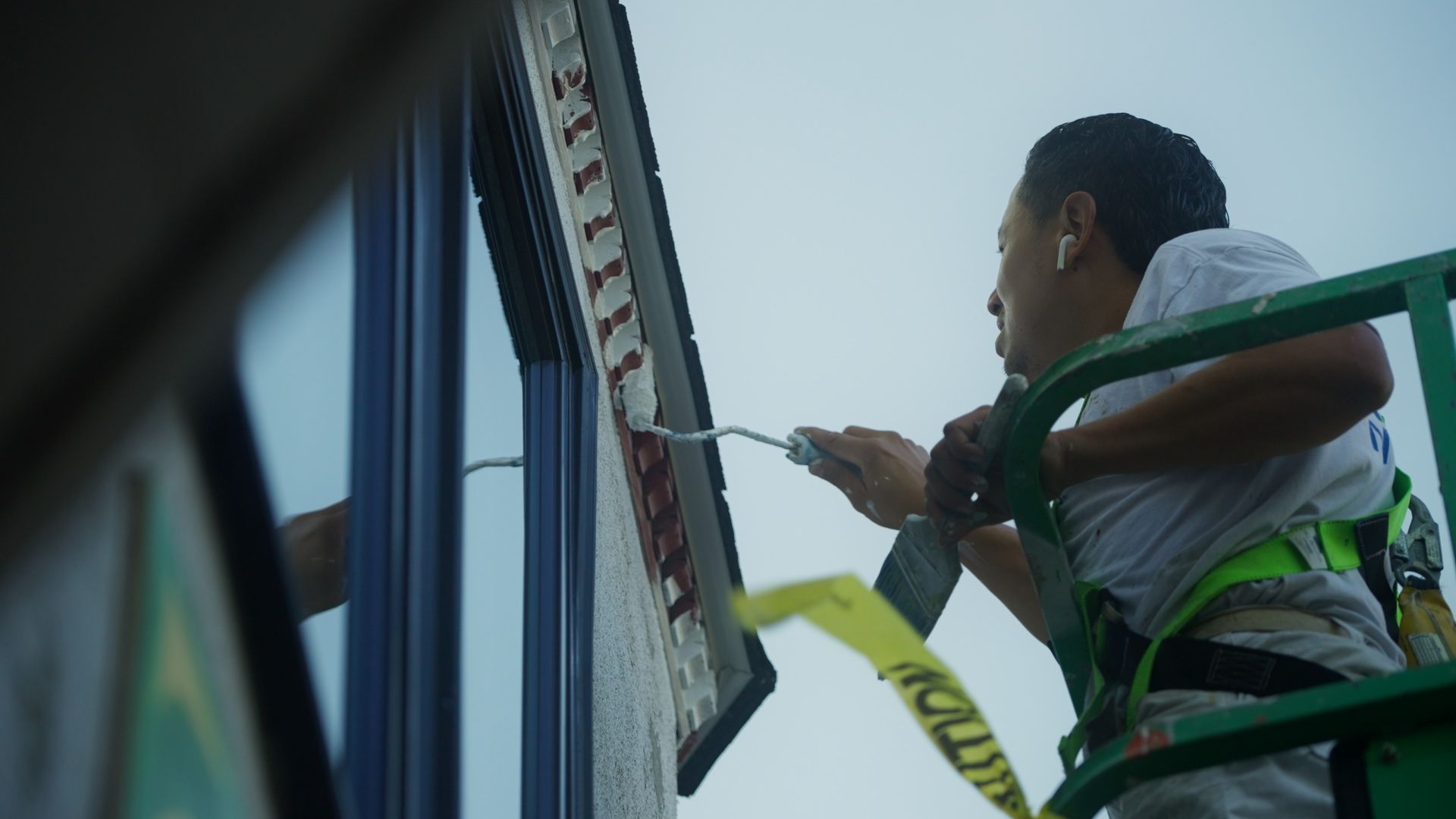 Person on a lift installing red decorative lights along a building's edge. The person is wearing a safety harness and focused on their work.