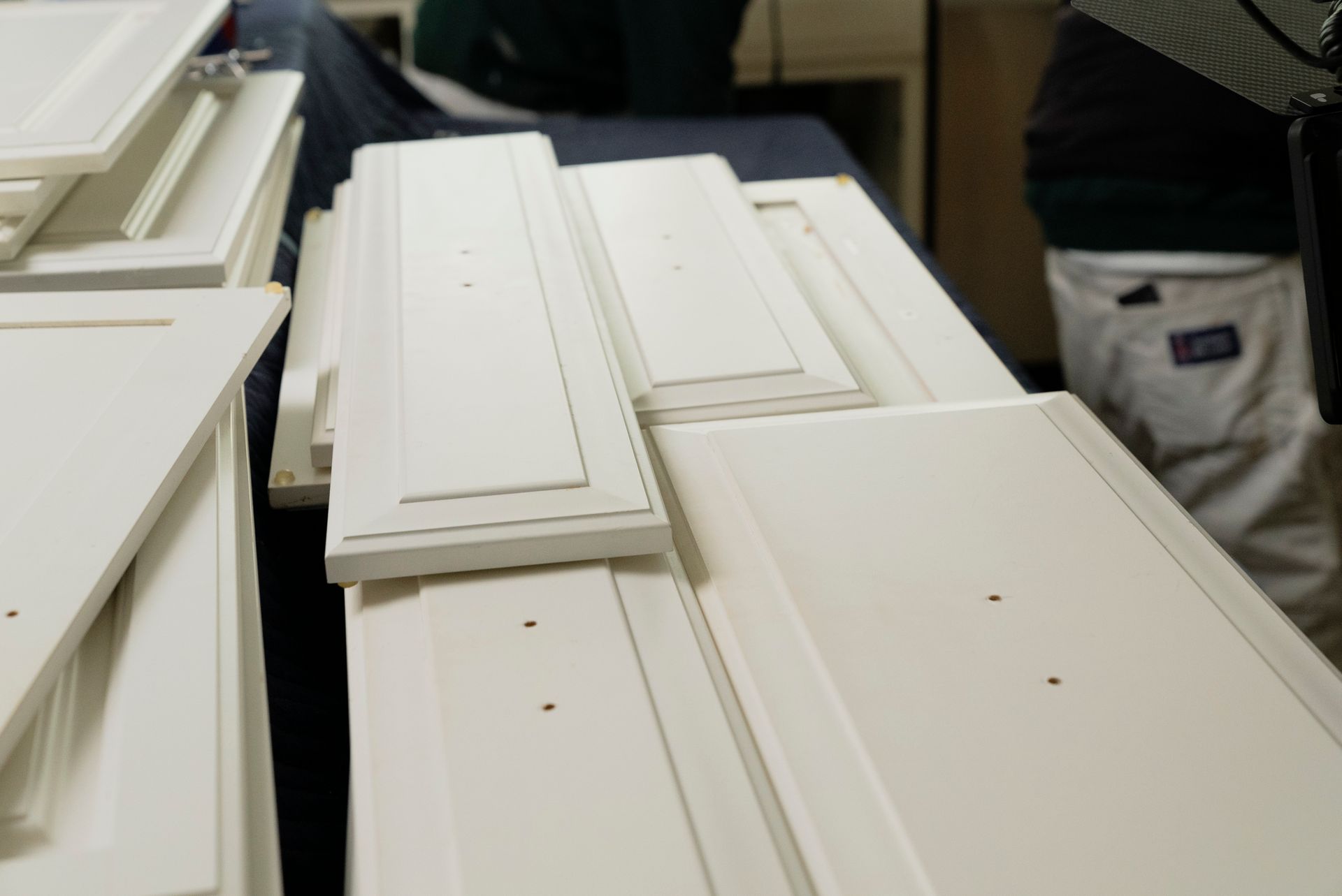 White cabinet doors stacked on a table, with a person in the background.