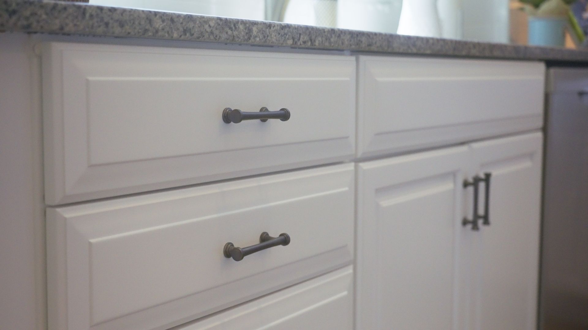 White kitchen cabinets with dark, textured hardware against a gray countertop.